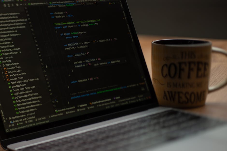 A close-up view of a laptop displaying lines of code on its screen, positioned on a wooden table. Next to the laptop, there is a coffee mug with a beige background and black text reading 'This coffee 